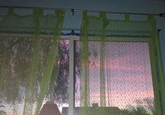 there is a window with green curtains in front of the windowsill and trees outside