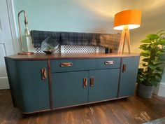 a blue sideboard with two drawers and a lamp on the table next to it