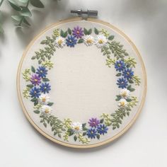 an embroidered hoop with flowers on it next to green leaves and a white wall hanging