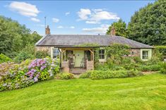 a small house sitting in the middle of a lush green field with flowers growing around it