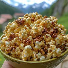 a hand holding a bowl full of popcorn with pecans in the middle and mountains in the background