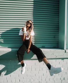 a woman sitting on the side of a building holding a cup of coffee in her hand