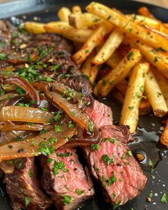 steak and french fries on a black plate with garnishes in the middle