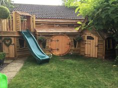 an outdoor play area with a slide and wooden barrels in the yard, surrounded by green grass