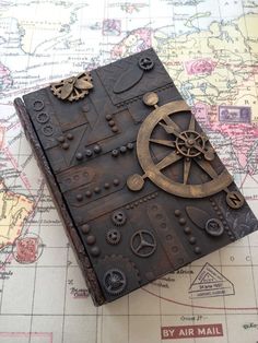 an old book is sitting on top of a map with gears and other things around it