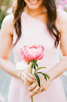 a woman holding a pink flower in her hand