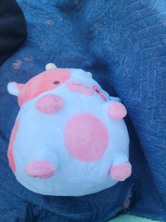 a blue and pink stuffed animal with spots on it's face sitting on a blanket