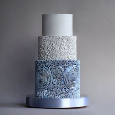 a three tiered blue and white cake on a silver plate with a gray background