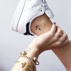 a woman's hand with a tattoo on her left arm holding up a white shoe