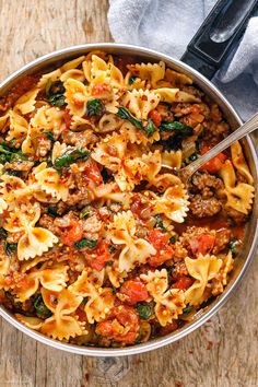 a pot filled with pasta and meat sauce on top of a wooden table next to a fork