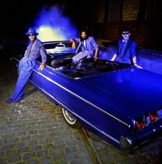 three men standing next to a blue car