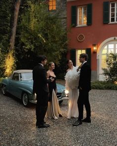 a group of people standing in front of a building with a car parked next to it