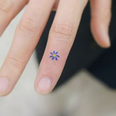 a person's hand with a tiny blue flower tattoo on their thumb and finger