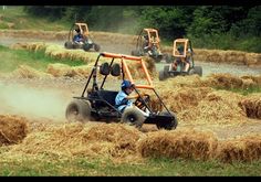 four people in buggies driving down a dirt road with straw bales on the ground