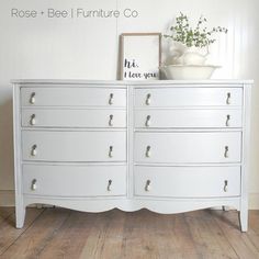 a white dresser sitting on top of a hard wood floor next to a vase with flowers