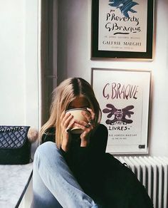 a woman is sitting on the floor with her hand to her face while holding a coffee cup in front of her face