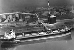 an old photo of a large boat in the water next to a factory and dock