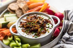 a white bowl filled with dip surrounded by veggies and crackers on a plate