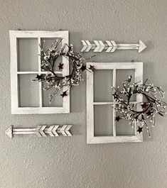 two white frames with wreaths and arrows hanging on the wall next to each other