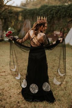 a woman in a black dress with a crown on her head holding flowers and ribbons