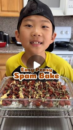 a young boy standing in front of an oven holding a tray with food on it