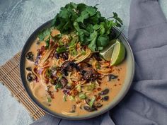 a bowl of soup with noodles, mushrooms and cilantro on a blue cloth