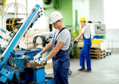 two men working in a factory, one is using a machine and the other is holding something