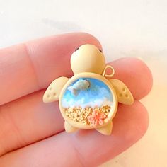 a tiny turtle brooch is sitting on someone's hand with sand in it