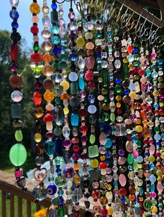 many different colored glass beads hanging from a wooden structure with trees in the back ground