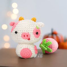 a small crocheted pig next to an orange on a table with lights in the background