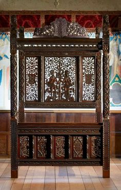 an ornate wooden bed in a room with paintings on the walls and wood flooring