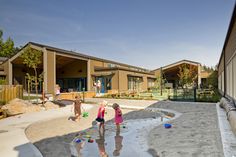 two children playing in the sand at a playground with their reflection on the wet ground