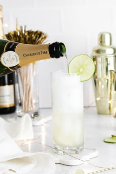 a bottle of champagne being poured into a tall glass filled with ice and limes