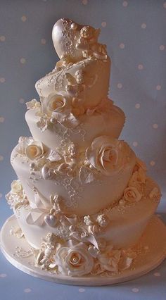 a three tiered wedding cake with white flowers and pearls on the top, sitting on a polka dot tablecloth