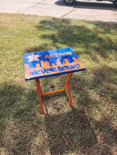 a blue and orange sign sitting on top of a grass covered field next to a parked car