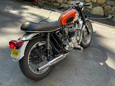 an orange and black motorcycle parked on the side of the road next to a stone wall