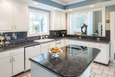 a large kitchen with white cabinets and black counter tops, along with a center island