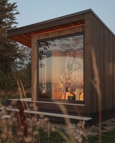 a woman is sitting in the window of a small wooden house with glass walls and doors