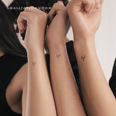 two women with matching tattoos on their arms, one has a cross and the other has an arrow