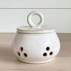 a white ceramic container with holes in the middle and a lid on it's side