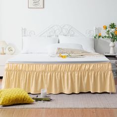 a white bed with yellow ruffled bedspread and pillows on the floor next to it