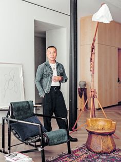 a man standing in front of a mirror next to a chair and table with a lamp on it