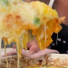 a person is taking a piece of pizza from a casserole dish with cheese and vegetables