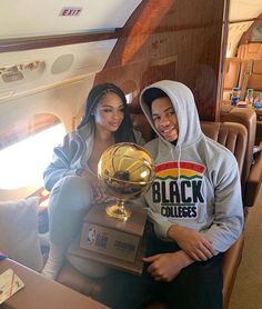 two people sitting on an airplane holding up a basketball trophy and posing for the camera