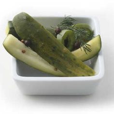 cucumbers and other vegetables in a bowl on a white surface with rosemary sprigs