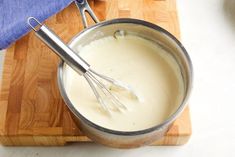 a wooden cutting board with a metal bowl and whisk in it