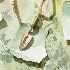 a green and gold necklace with a knife on it's end sitting on a piece of paper