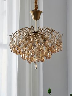 a chandelier hanging from a ceiling in front of a window with white curtains