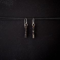 two silver earrings hanging from a black leather cord on a black surface with white stitching