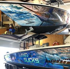 two boats are hanging from the ceiling in a garage, one is painted with an ocean theme